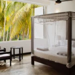 Open-air Deluxe Room with canopy bed surrounded by palm trees